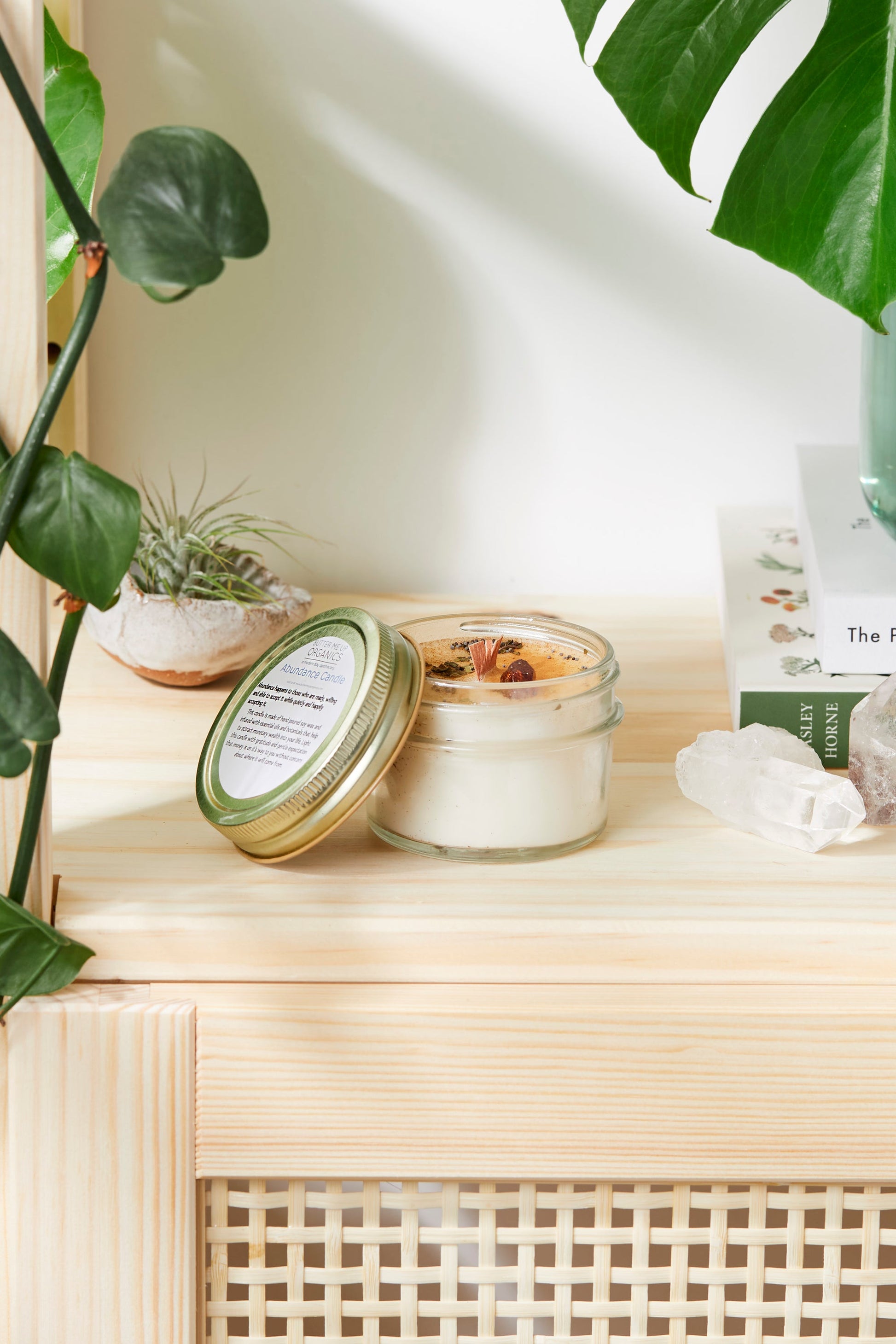 Abundance Ritual Candle in a glass jar, hand-poured soy wax with wood wick, surrounded by greenery and books.